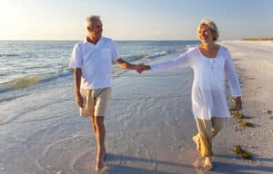 Senior pair strolling along sunlit seashore